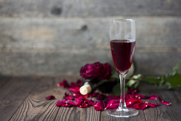 glass of wine and a rose and rose petals on wooden background