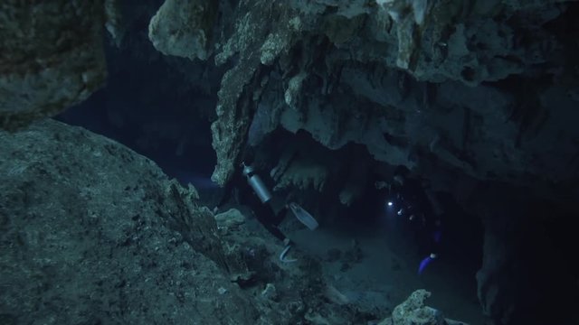 two divers underwater with flashligh swiming through stalagmite in cenote cave dos ojos