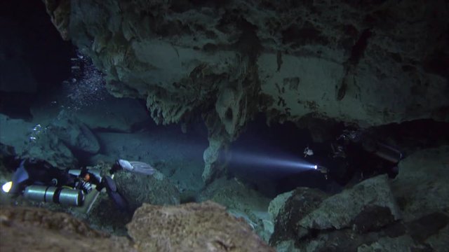 group of divers with flashligh in dark cenote cave dos ojos