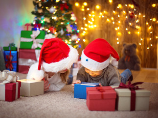 Fototapeta na wymiar Boy and girl lying on the floor with presents near christmas tree