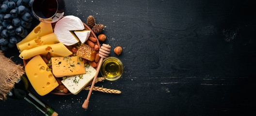 Assortment of cheeses, a bottle of wine, honey, nuts and spices, on a wooden table. Top view. Free space for text. - obrazy, fototapety, plakaty