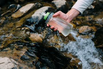 tourist pouring water from mountain river into bottle, hand close-up