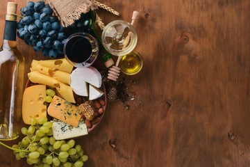 A bottle of wine, and a large assortment of cheeses, honey, nuts and spices, on a wooden table. Top view. Free space for text.