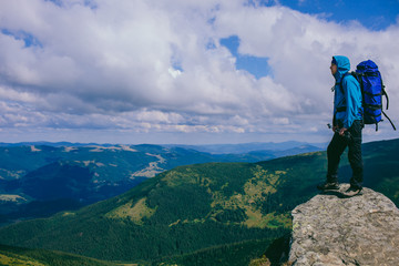 Naklejka premium man traveler standing on the top of the mountain and looking into the mountainous landscape. Adventure and active recreation in the mountains