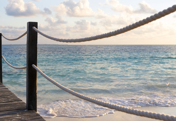 View to the sea behind the ropes on wooden pier. Sunrise time on the Caribbean ocean shore.