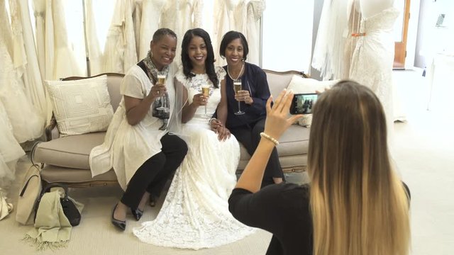 Medium shot of a sales assistant taking photos of customers in a bridal salon