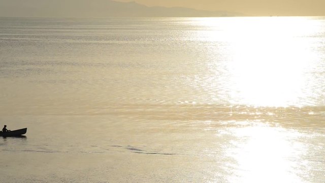Un mare piatto e luccicante color oro attraversato da una barca a motore con pescatore
