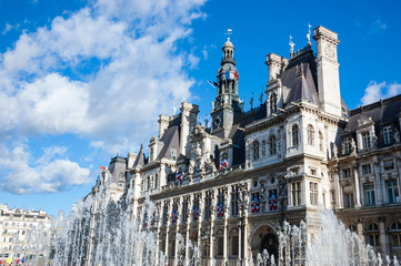 Paris City Hall (Hotel de Ville) decorated with flags and fountains in sunny day.