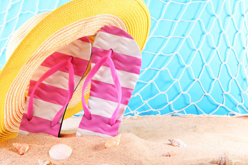 Flip flops with yellow hat and seashells on the beach sand