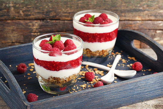 Dessert with raspberries and granola in glasses on grey wooden table
