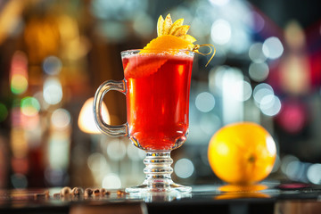 Closeup glass of red cocktail decorated with orange and apple slices at bright bar counter background.