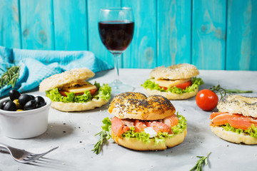 Bagels with salmon, vegetables, cream-cheese and glass of red wine on grey concrete background