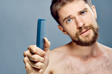 A young guy with a beard on a gray background holds a comb