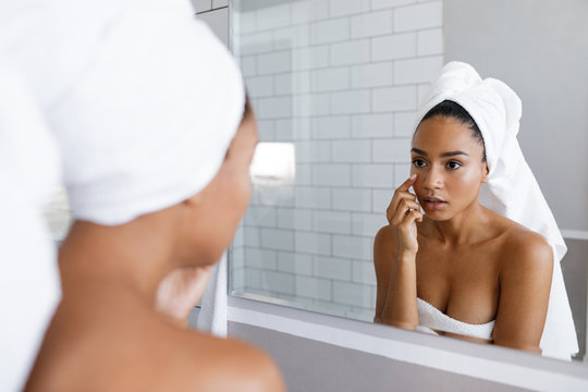 Close up shot of an attractive young woman inspecting her skin, standing in front of the bathroom mirror