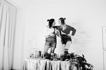Two fun beautiful girls friends wear in overalls jeans shorts and gaiters against table with new...
