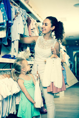 Naklejka premium portrait of woman and girl shopping white baby apparel in clothes store