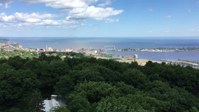 Aerial view of Duluth Minnesota high above dark green trees with Lake Superior and city in far background on sunny afternoon in July.