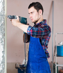 confident professional builder drilling hole in wall with perforator