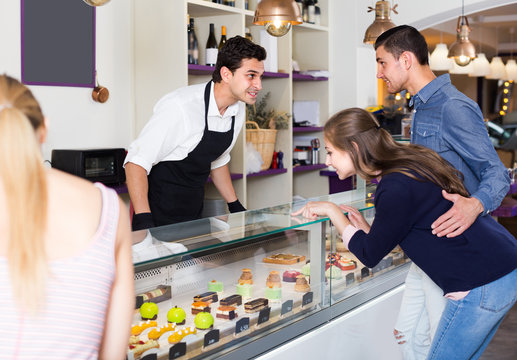 Family couple with female friend are choosing delicious cakes from showcase