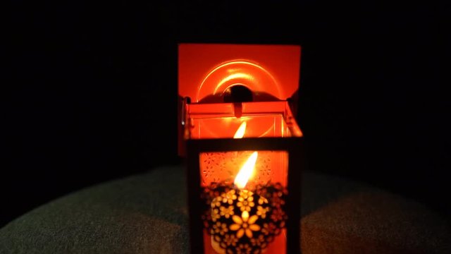The yellow candle went out in a red metal lantern with a delicate heart on its side on a black background, slow motion.