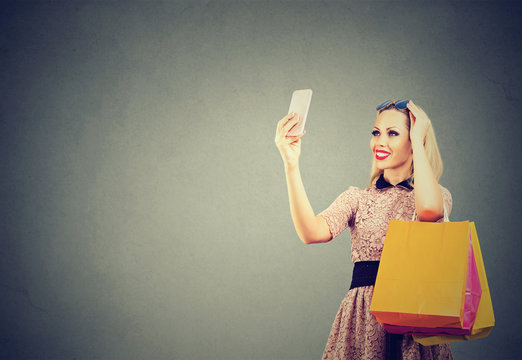 Beautiful woman shopping online taking selfies on mobile phone. Fashion girl with colorful bags looking at cellphone.
