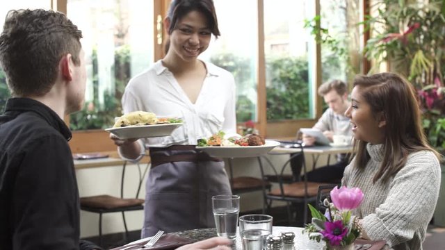 Medium shot of a waitress serving food for a couple