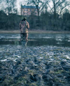 Fisherman near the river.  Muddy riverbank.  Focus to mud. The model is not visible and not recognizable. Vintage image effect.