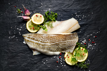 Fresh fish,  raw cod fillets with addition of herbs and lemon slices on black stone background, top view   © zi3000