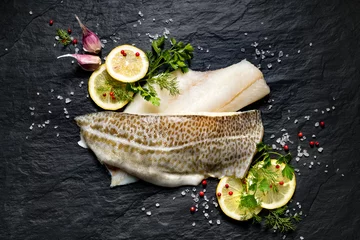  Fresh fish,  raw cod fillets with addition of herbs and lemon slices on black stone background, top view   © zi3000