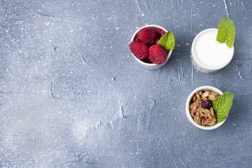 a glass with yoghurt, muesli and berries on a gray background and a white plate