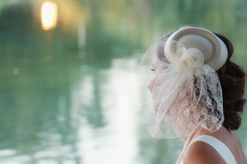 Vintage bridal wedding hairstyle of blonde bride with little hat and short veil close up water background