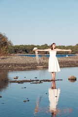 Happy young bride standing barefoot in lake shore with wedding dress and holding wedding bouquet and spread her arms and feeling freedom