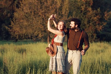 vintage dressed young couple dancing romantically in green grass at sunset