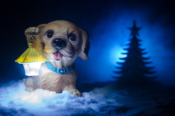 Toy dog - a symbol of the new year under the snow against the background of fir branches. Toy's dog as a symbol of 2018 New Year with a Christmas attributes the new year's inscription