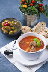 tomato soup in a white plate with meat balls, on a stone background with bread and olives