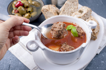 tomato soup in a white plate with meat balls, on a stone background with bread and olives