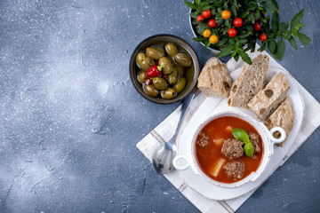 tomato soup in a white plate with meat balls, on a stone background with bread and olives