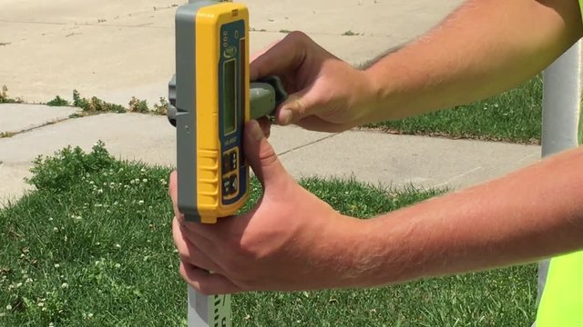 Man working in construction industry twists side of ground leveling device in bright sunlight.  