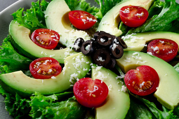 Sliced avocado with cherry tomatoes, olives, salad leaves and ch