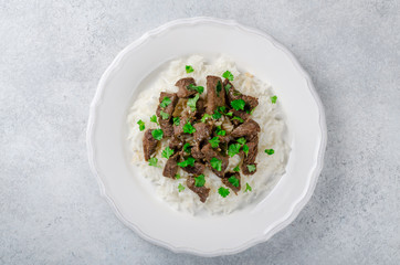 Cooked rice and fried beef with parsley on a white plate on a li