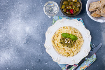 plate with pasta with pesto sauce and olives on a stone background