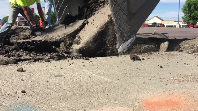 Powerful display of massive power with construction backhoe bucket ripping up a large section of blacktop in bright sunlight.