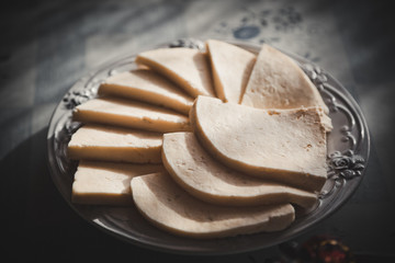 Homemade cheese, cut into pieces, lies on a plate on a wooden table