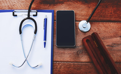 Doctor workplace. Stethoscope with notebook and pencil on the wooden table. Medical concept