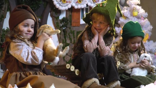 Two girls are playing with fluffy rabbits and the boy with a smile looks at them, waiting for Christmas, slow motion