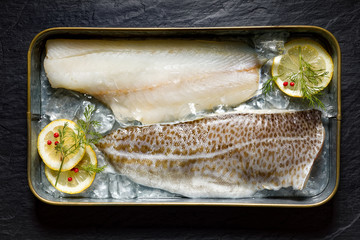 Fresh fish, cod fillets on ice with lemon slices, dill and red peppercorns, top view, horizontal...