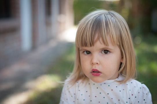 Two year old girl with lipstick, confused looking at camera
