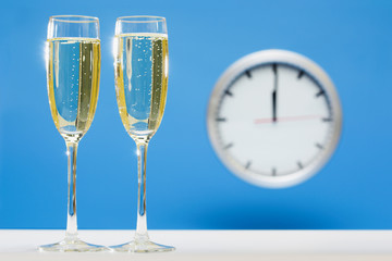 series of a plain simple clock on New Years Eve, before and during Midnight, on bright blue background: champagne glasses are filled