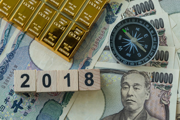 Fototapeta na wymiar Wooden block with number 2018, gold bullion and compass on pile of japanese yen banknotes as year 2018 financial safe haven or tax concept
