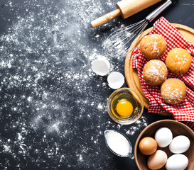 Baking ingredients. Bowl, eggs, flour, eggbeater, rolling pin and eggshells on black chalkboard from above.